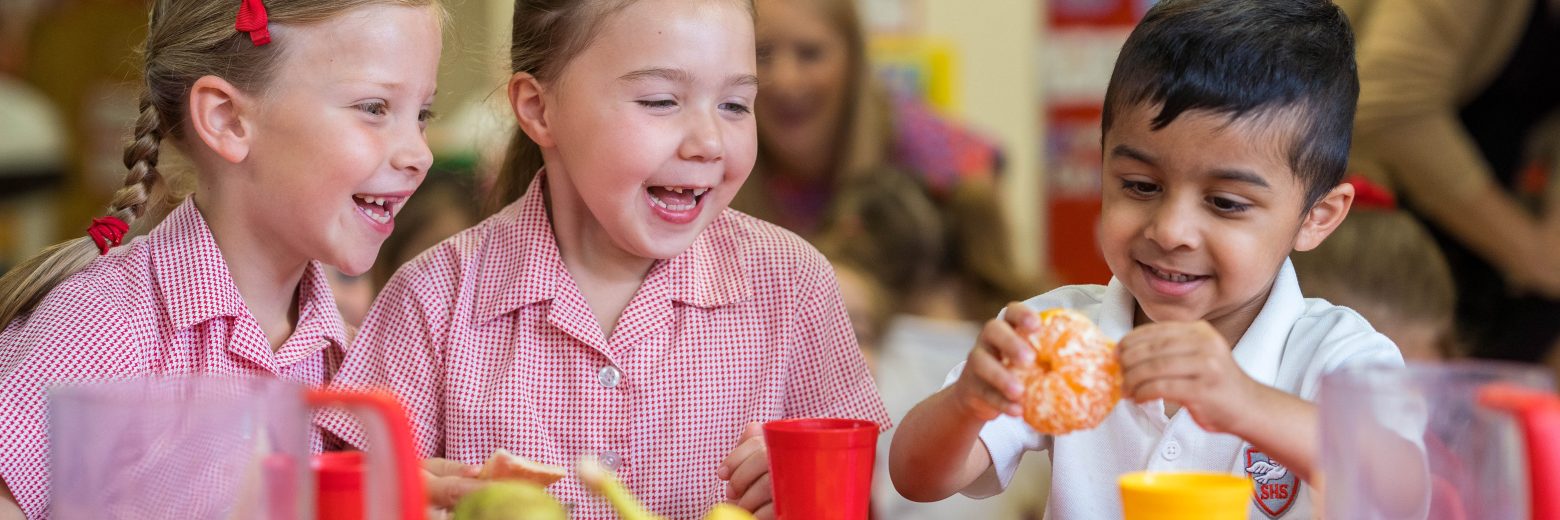 3 students eating different fruits, as a child unpeels an orange