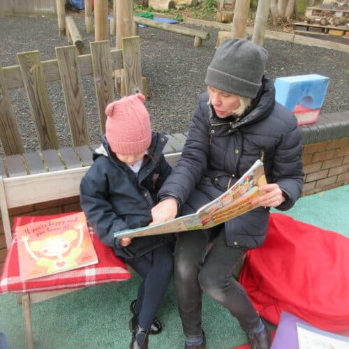 nursery student reading with her teacher outside