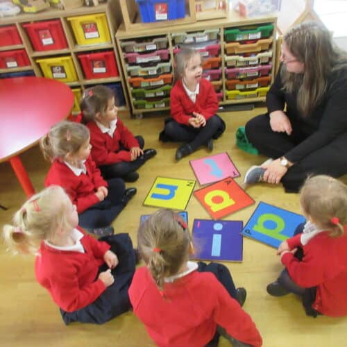 nursery students sat on the floor near a pile of wooden letters