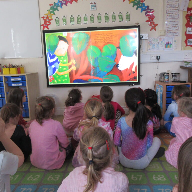 Group of young students sitting on the floor and facing a large colorful painting displayed on an interactive whiteboard in a classroom.