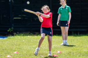 girl wearing red top hitting rounders ball
